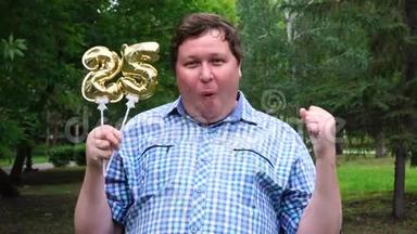 大个子拿着金色的气球，在户外做25号。 25周年庆祝晚会